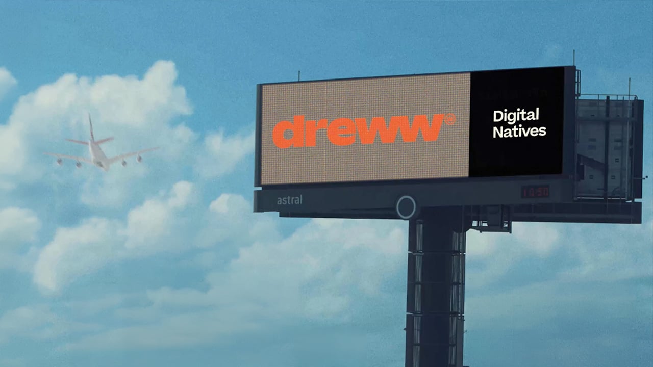 Dreww ‘Digital Natives’ billboard against a blue sky with a plane flying past