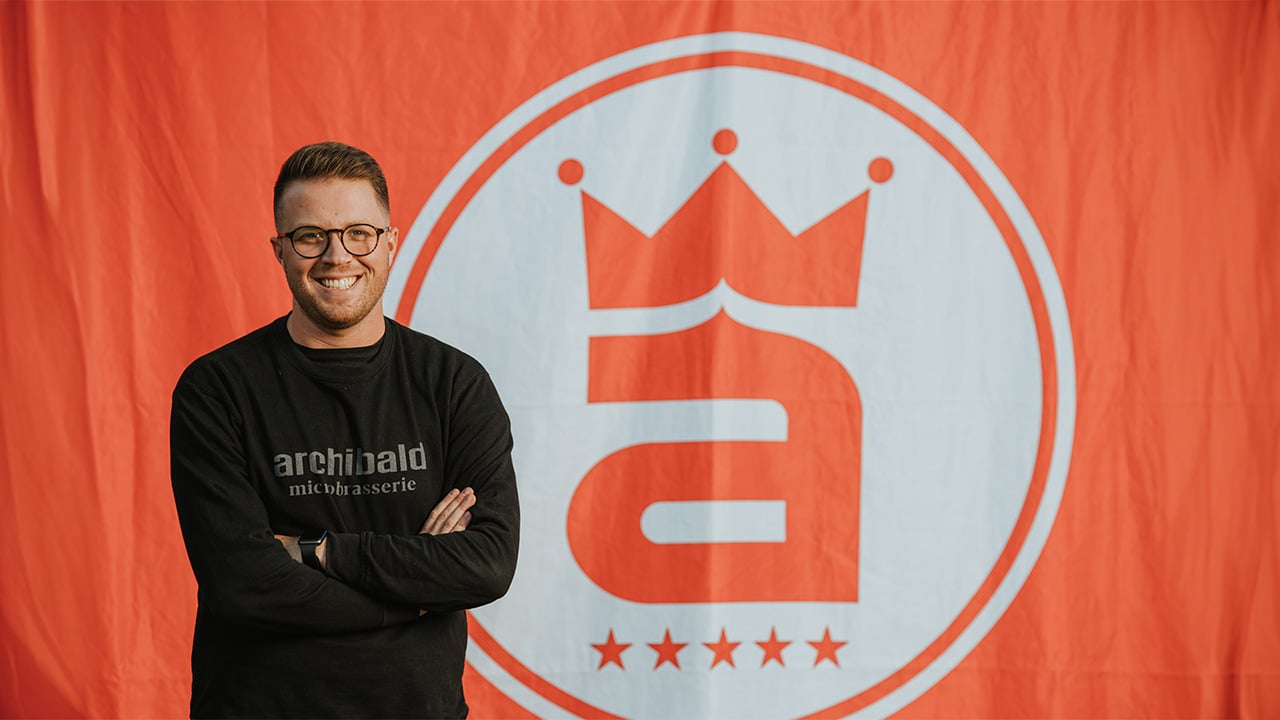 Etienne Dancosse standing in front of the Archibald logo