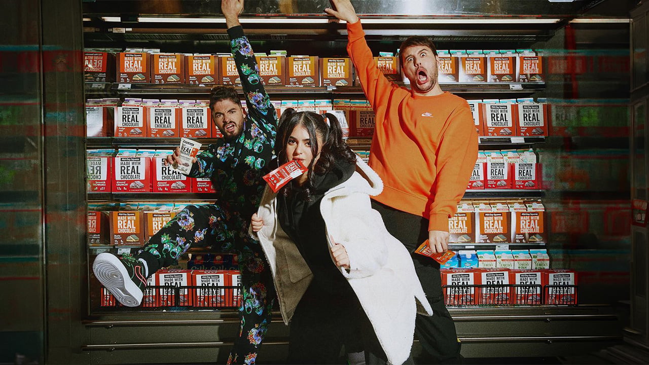 Mid-Day Squares founders posing in front of a grocery fridge stocked with their chocolate bars