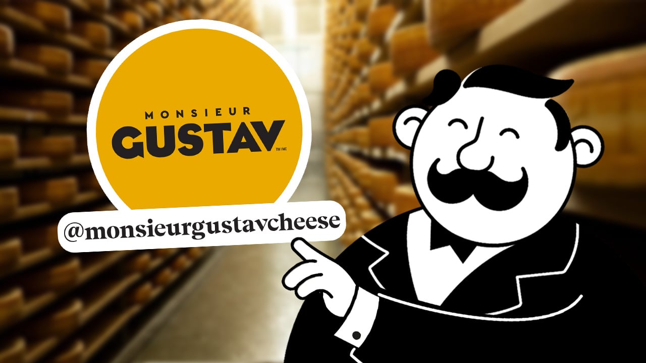 La mascotte de Monsieur Gustav pointe le logo de la marque et l'identifiant @monsieurgustavcheese dans une cave d'affinage